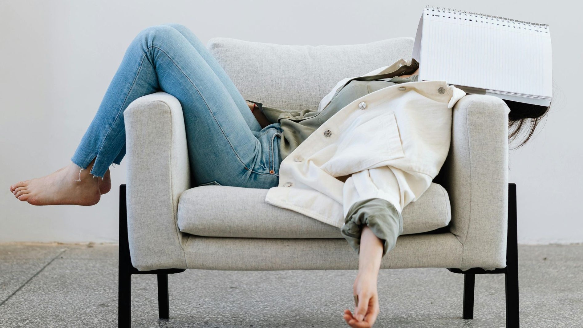 a girl lying on sofa with a notebook covering her head
