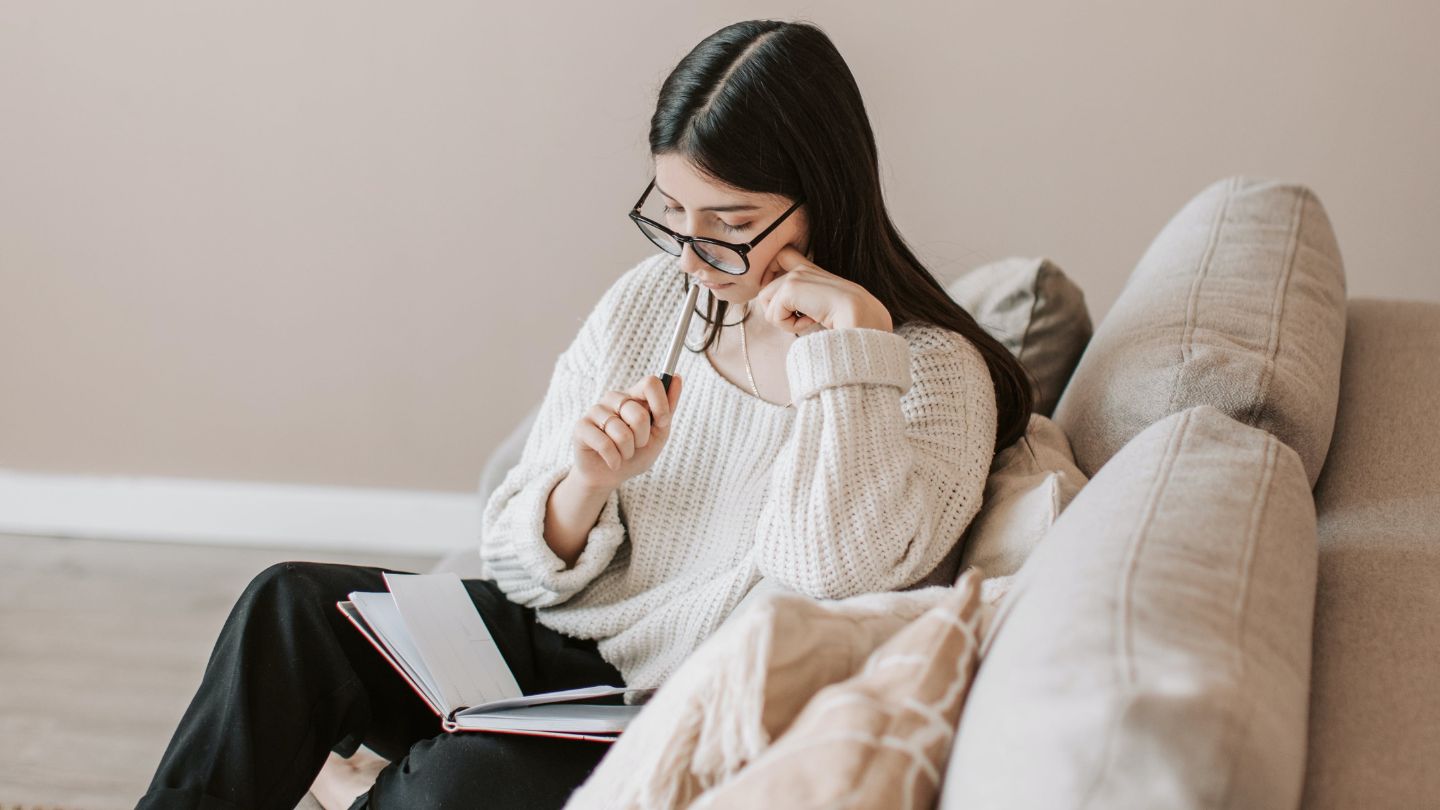a girl wearing glasses journaling on the sofa